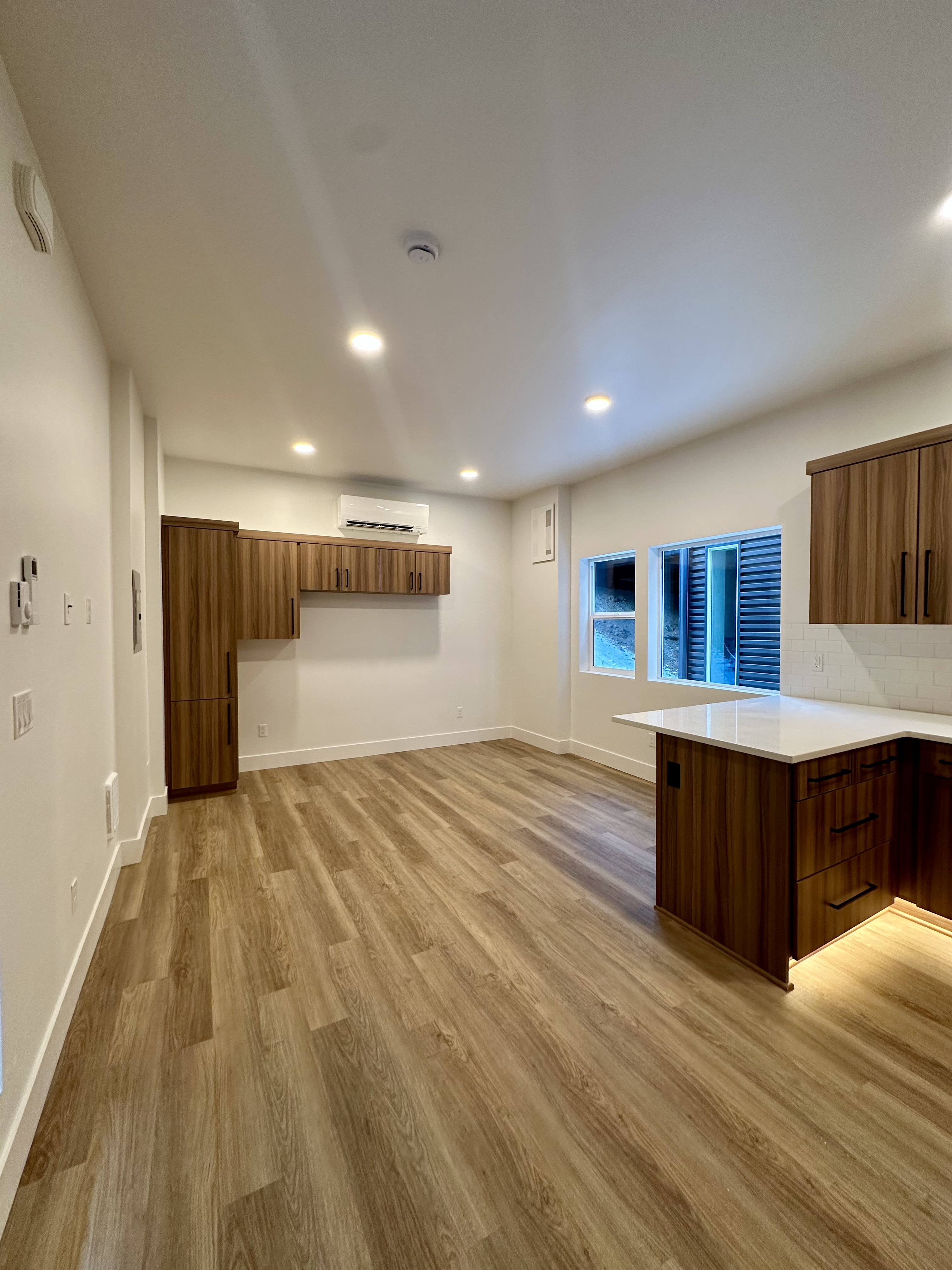 Kitchen with wood cabinets, white countertops, windows, recessed ceiling lights, and wood-patterned flooring.