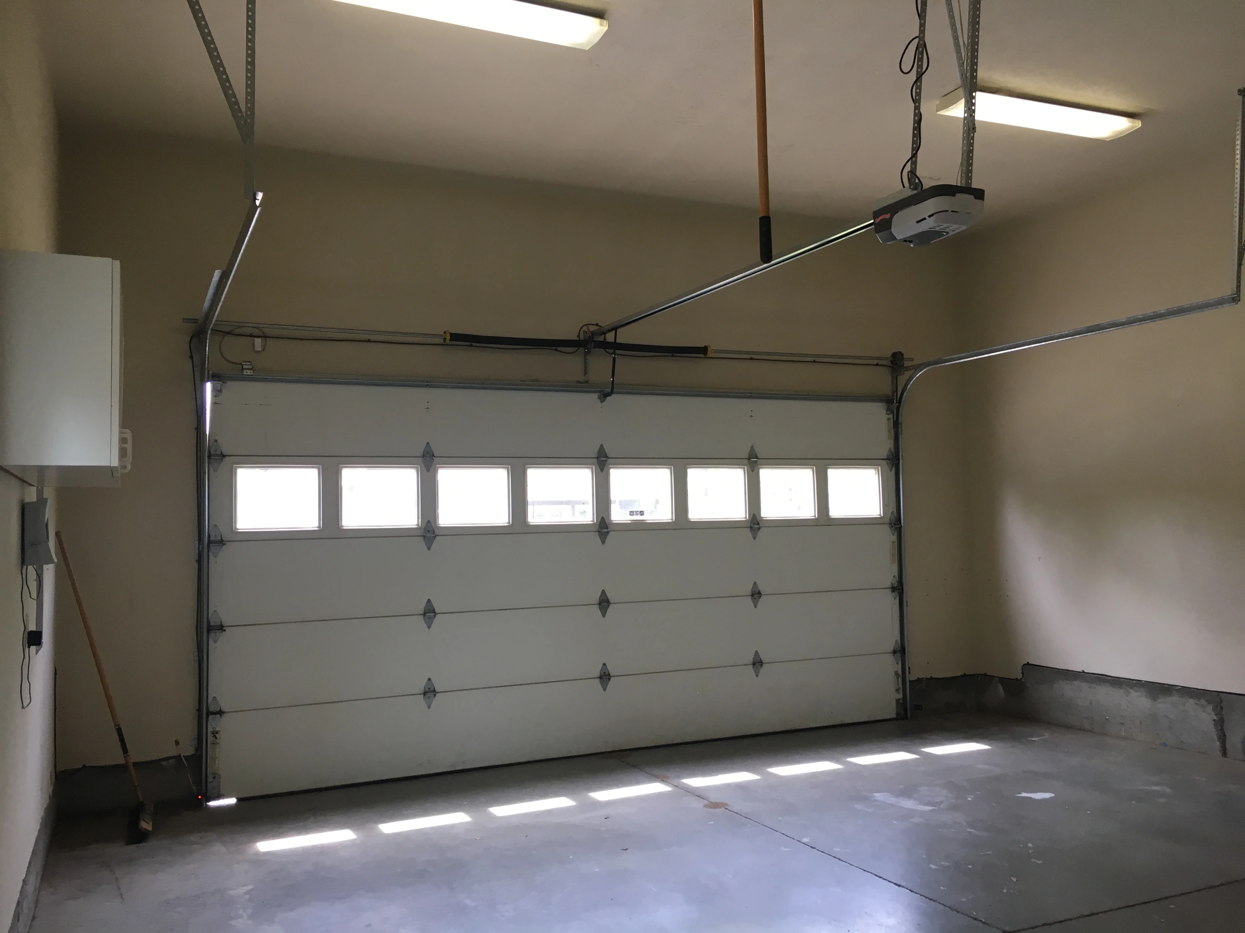An empty garage with a closed sectional door, a row of windows, and ceiling-mounted opener rails.