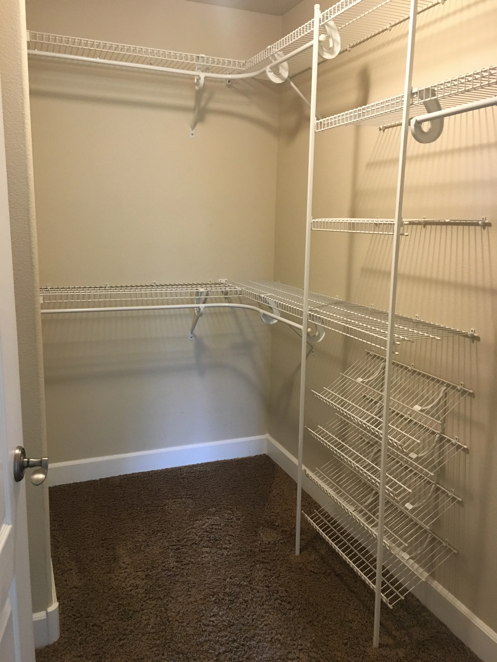 An empty carpeted closet has white wire shelves and hanging rods along three walls.