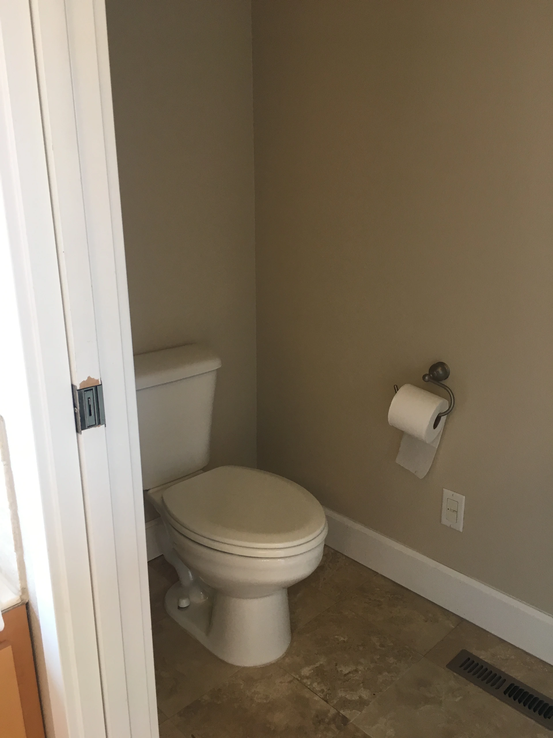 A toilet with its lid closed sits beside a wall-mounted toilet paper holder in a small room with tiled flooring.