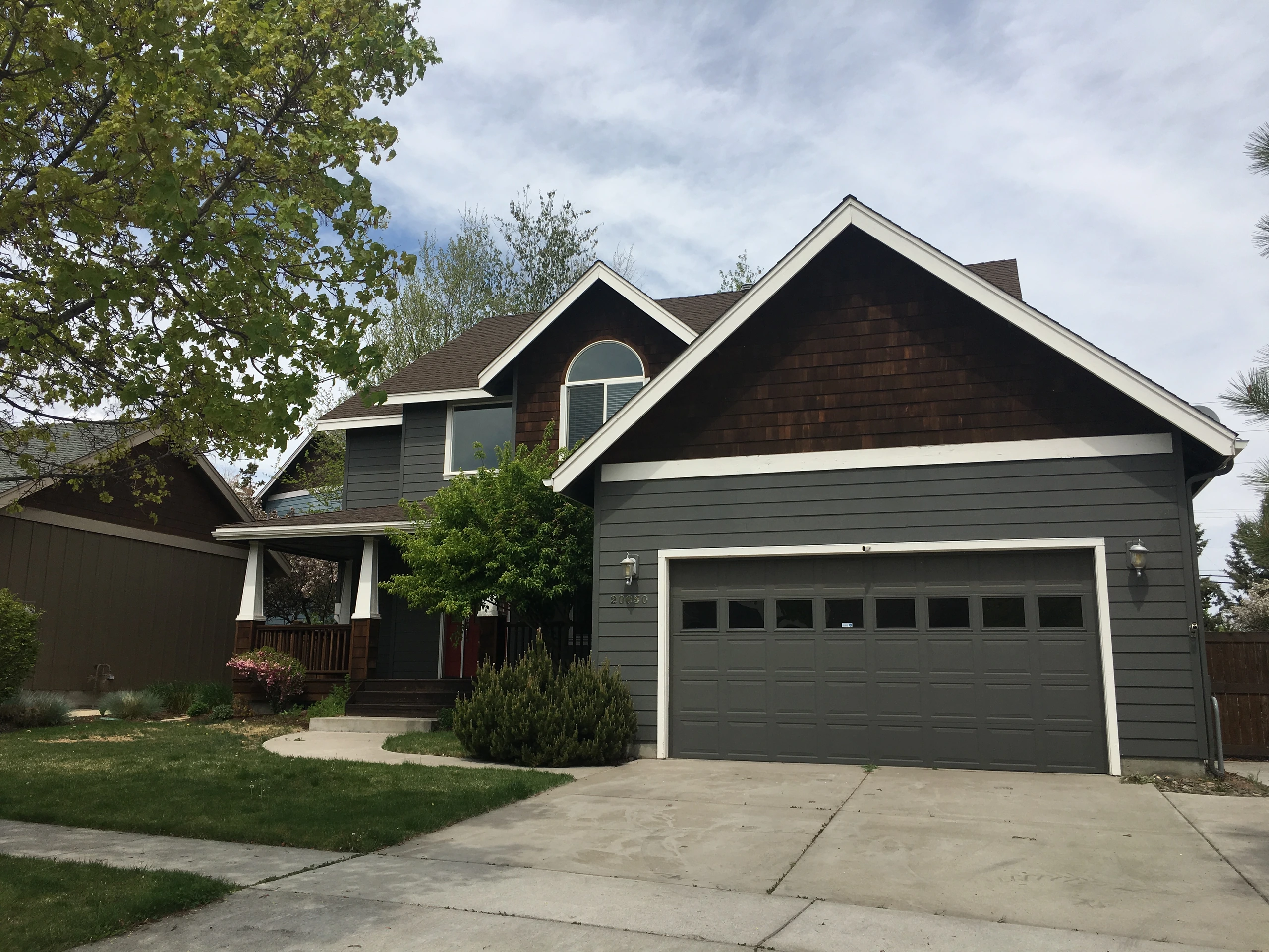 A two-story gray house has dark gables, white trim, a double garage, and a covered front porch.
