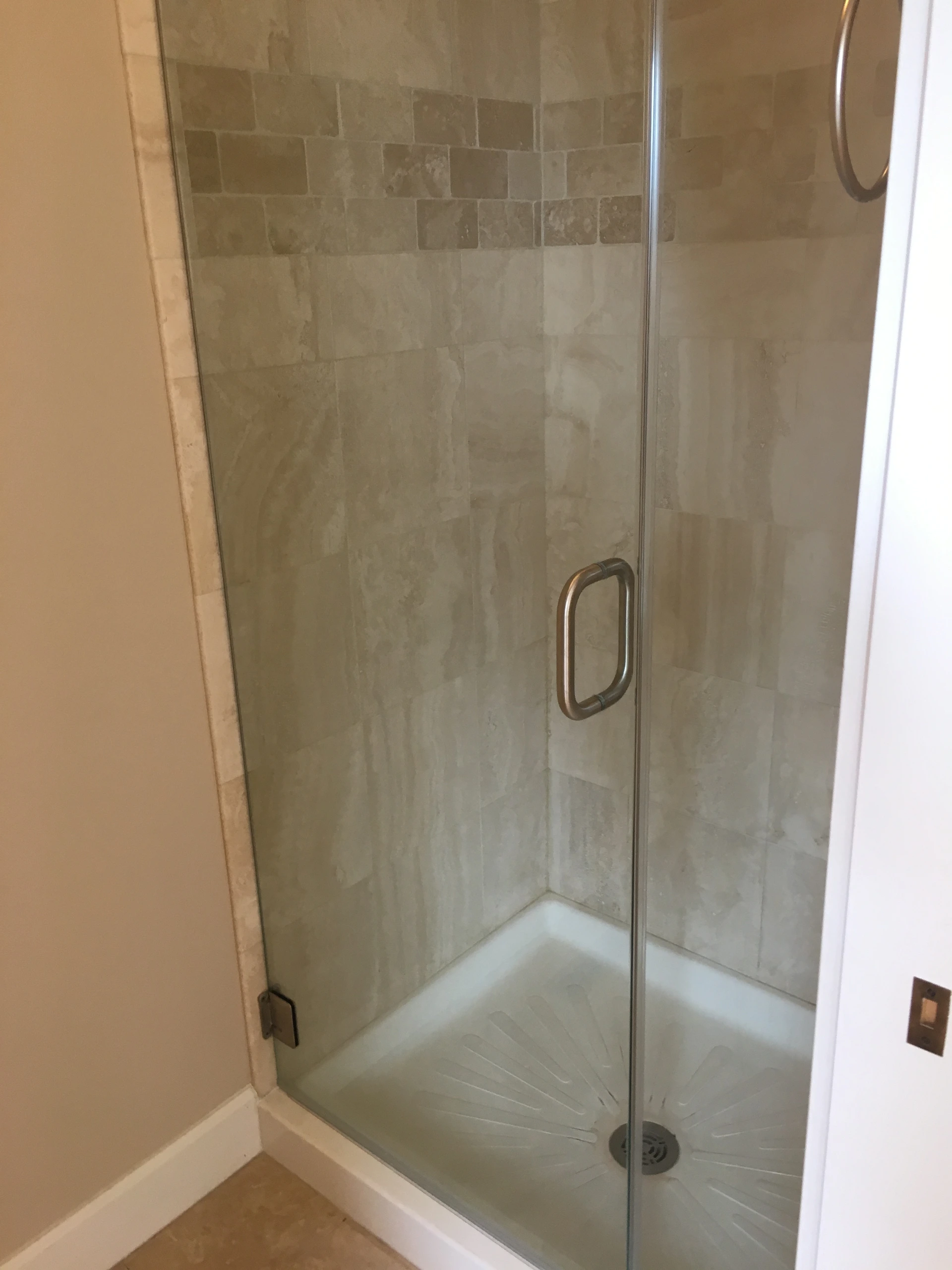 A glass shower enclosure has a metal handle, tiled walls, and a white shower base with a drain.
