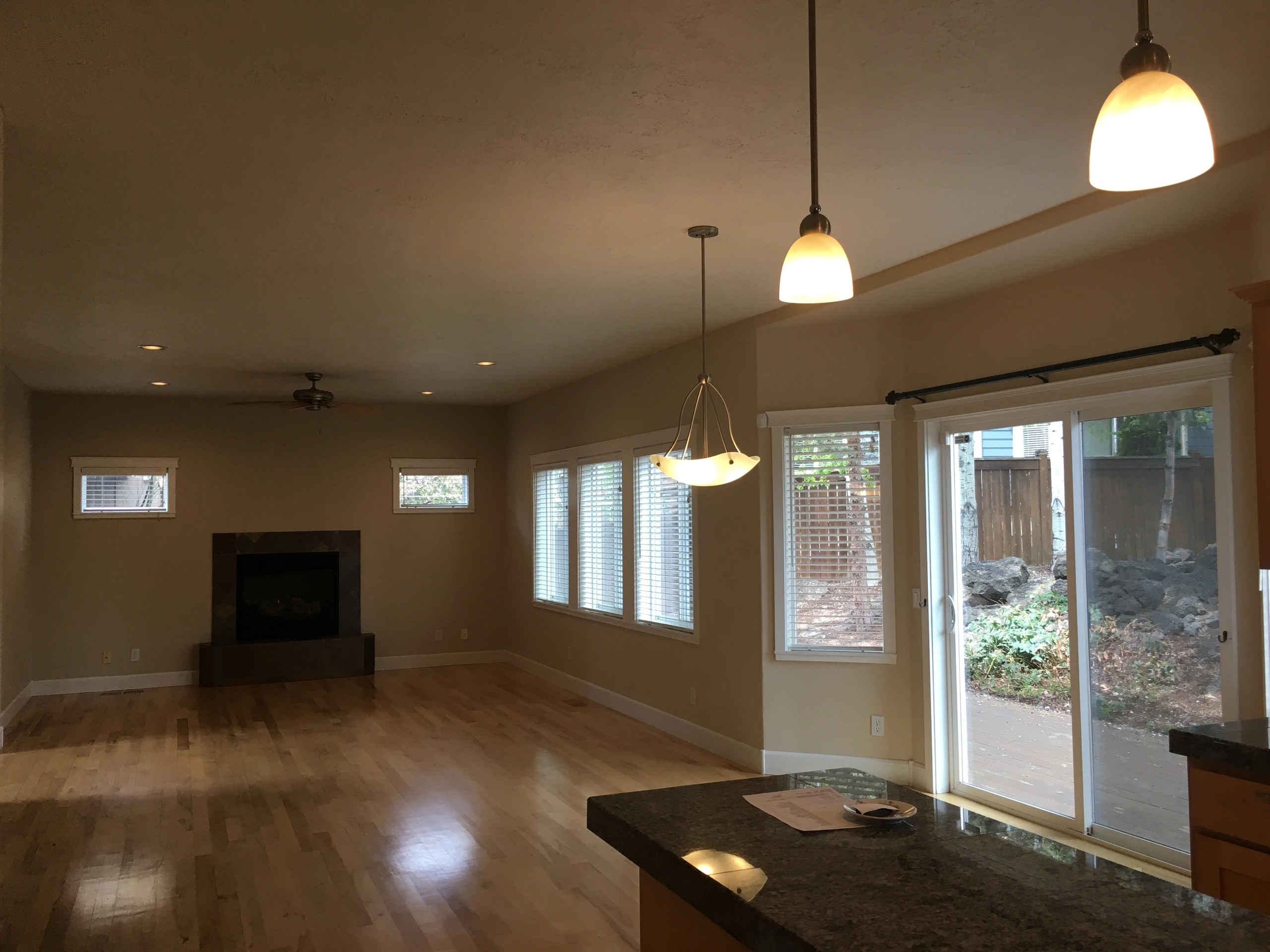 An open room has wood flooring, a fireplace, several windows, sliding glass doors, and hanging lights.