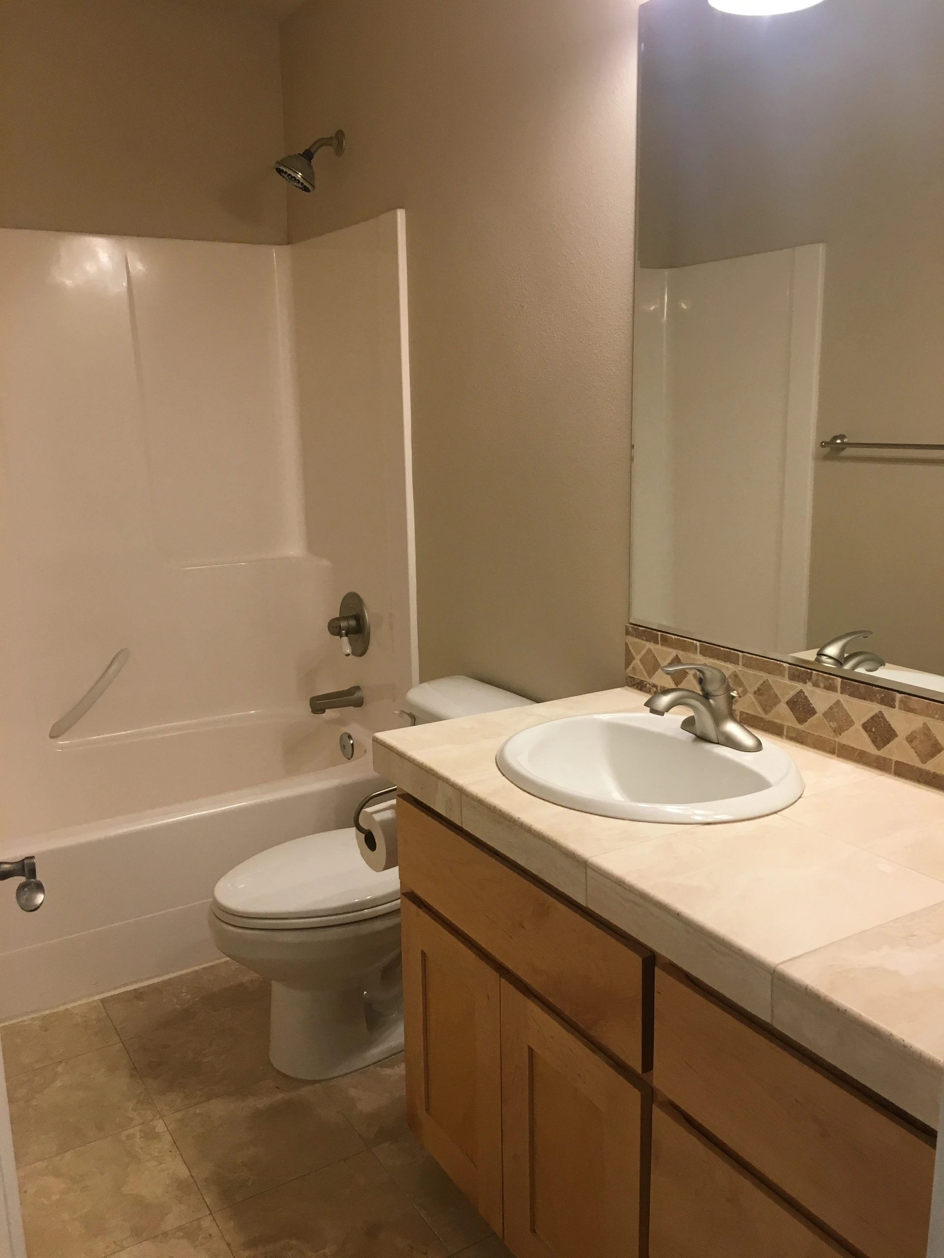 A bathroom with a white tub and shower, toilet, and a wood vanity with an oval sink beneath a large mirror.