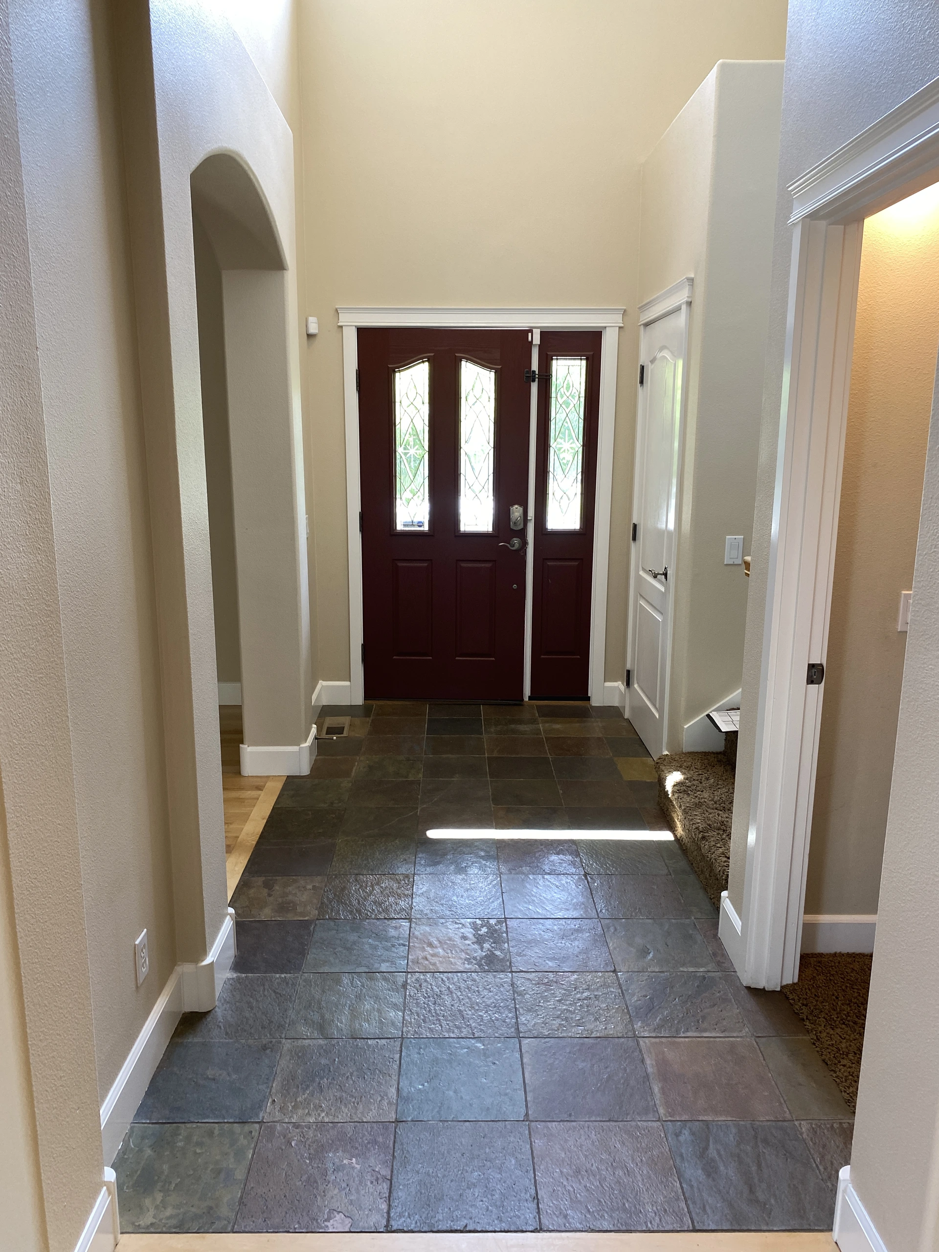 A tiled entry hall with dark double doors and a matching narrow side door, all with patterned glass panels.