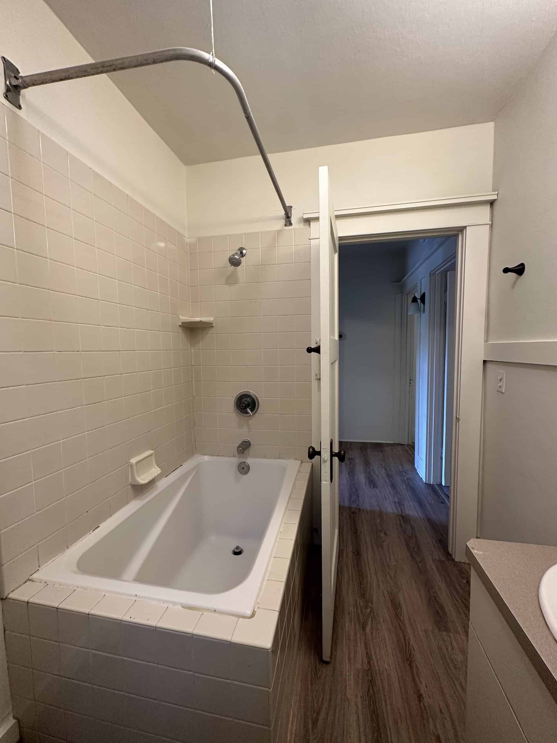 A white bathtub with tiled walls and a curved shower rod stands beside an open doorway.