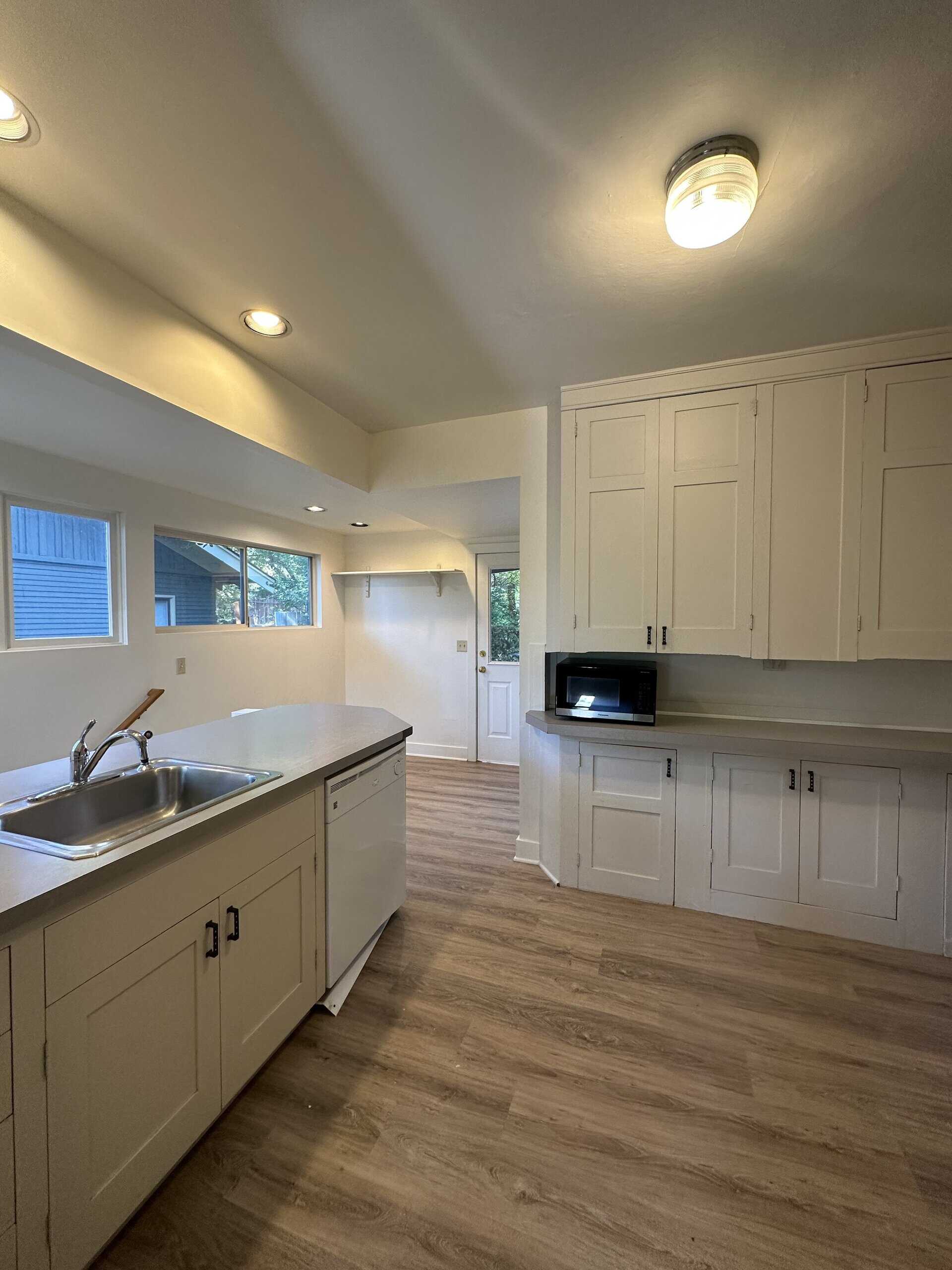 A kitchen with white cabinets, a sink island, a microwave, windows, and wood-patterned flooring.