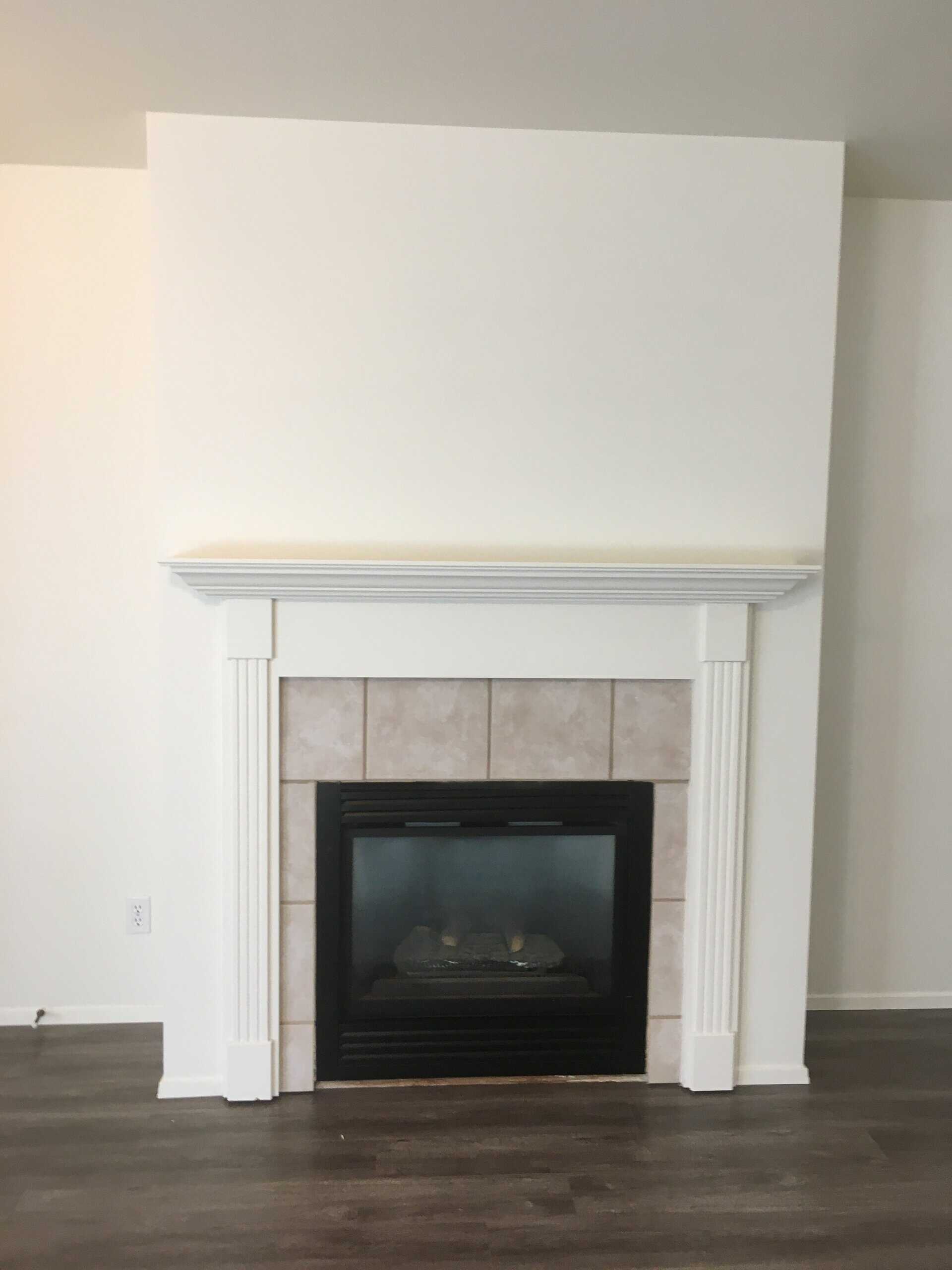 A black fireplace insert sits within a light tiled surround beneath a white mantel, above a dark wood floor.