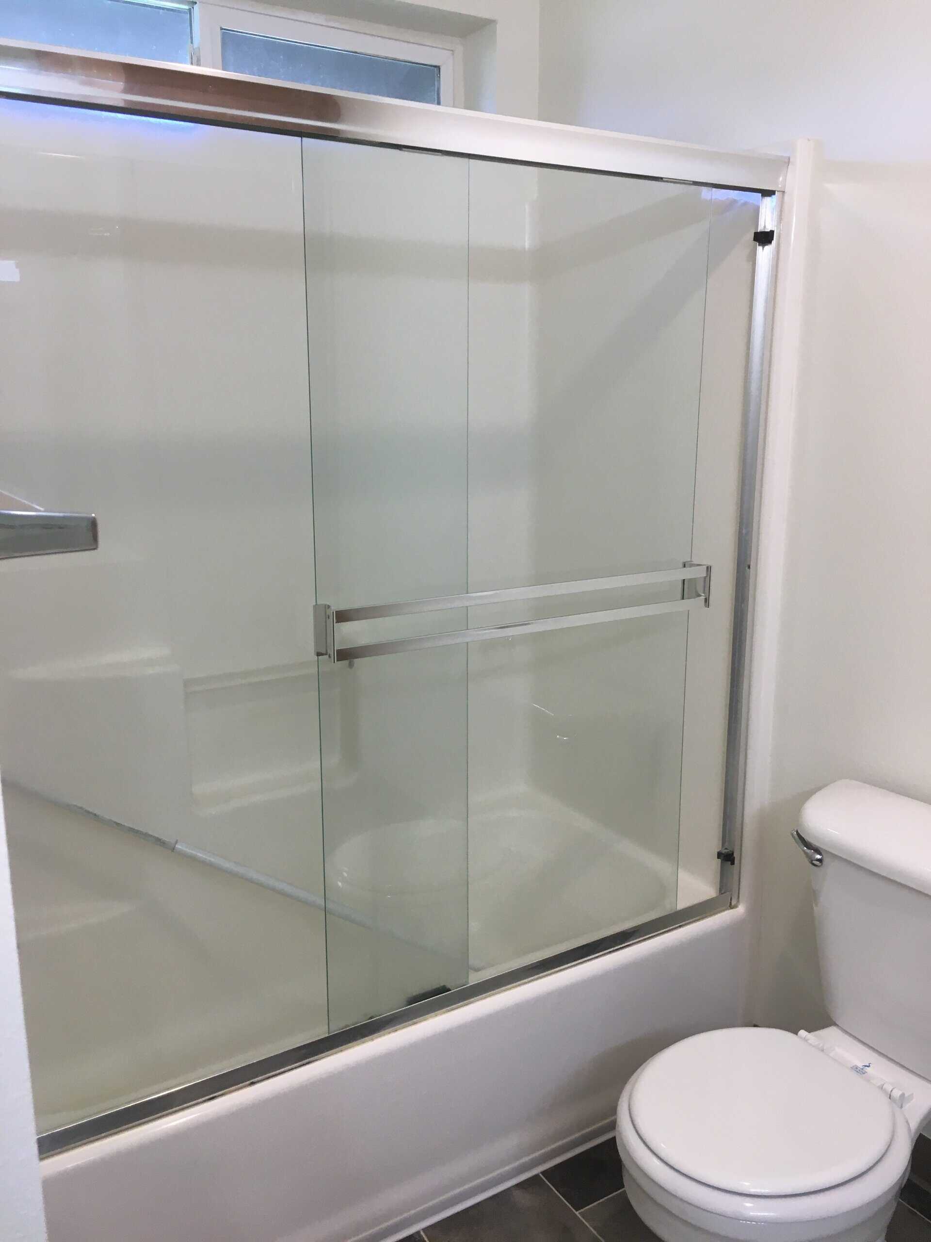 A bathtub with sliding glass panels and metal rails sits beside a white toilet.