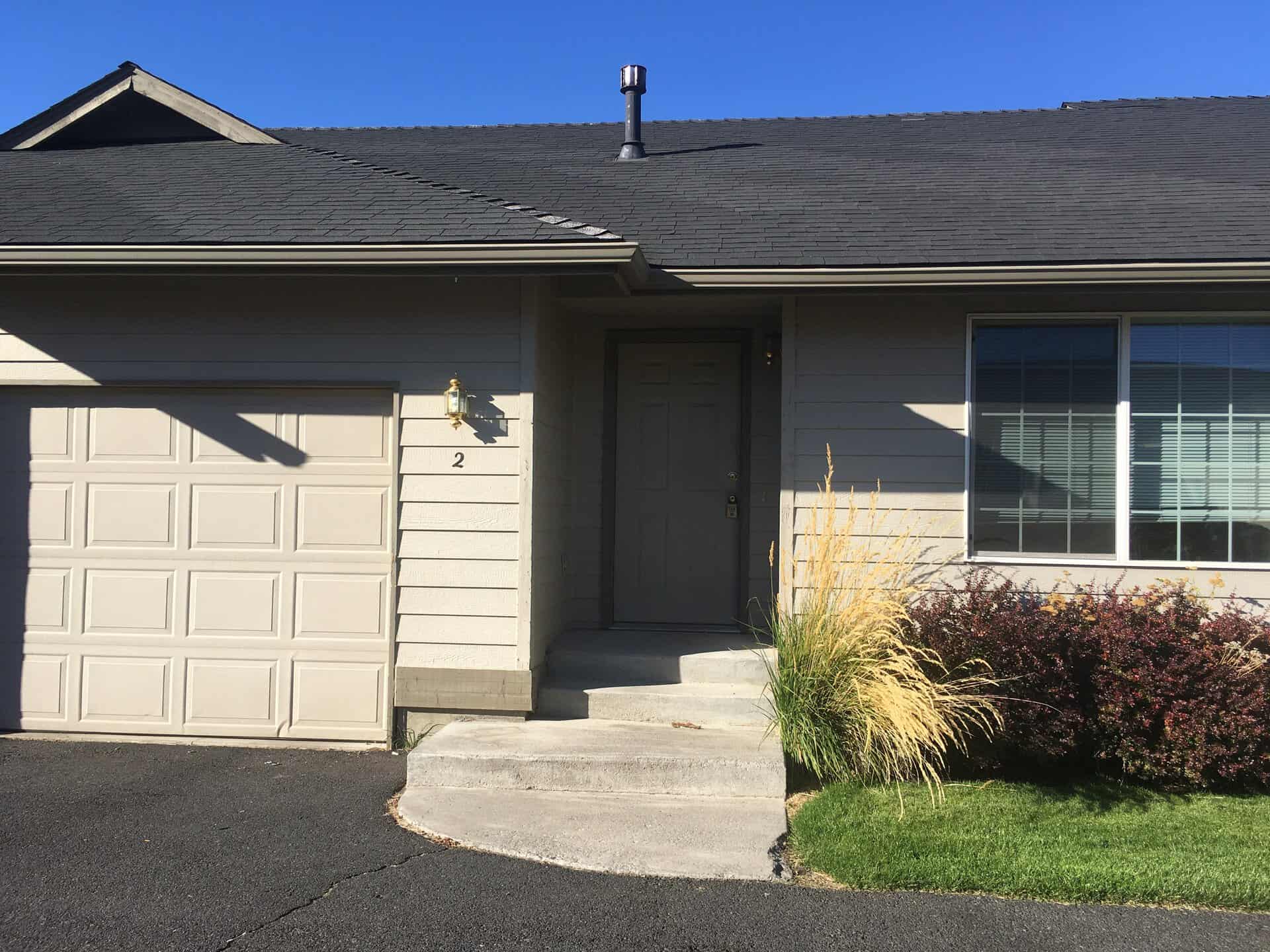 A house exterior with a paneled garage door, recessed entry, front window, concrete steps, and landscaping.