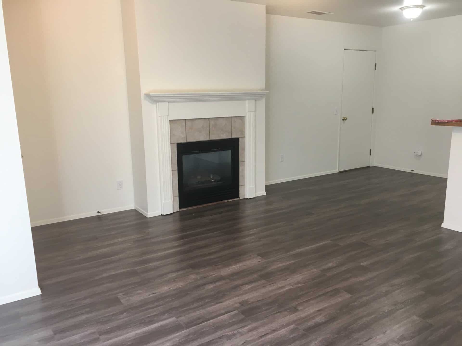 An empty room has dark plank flooring, a tiled fireplace with a white mantel, and a closed door.