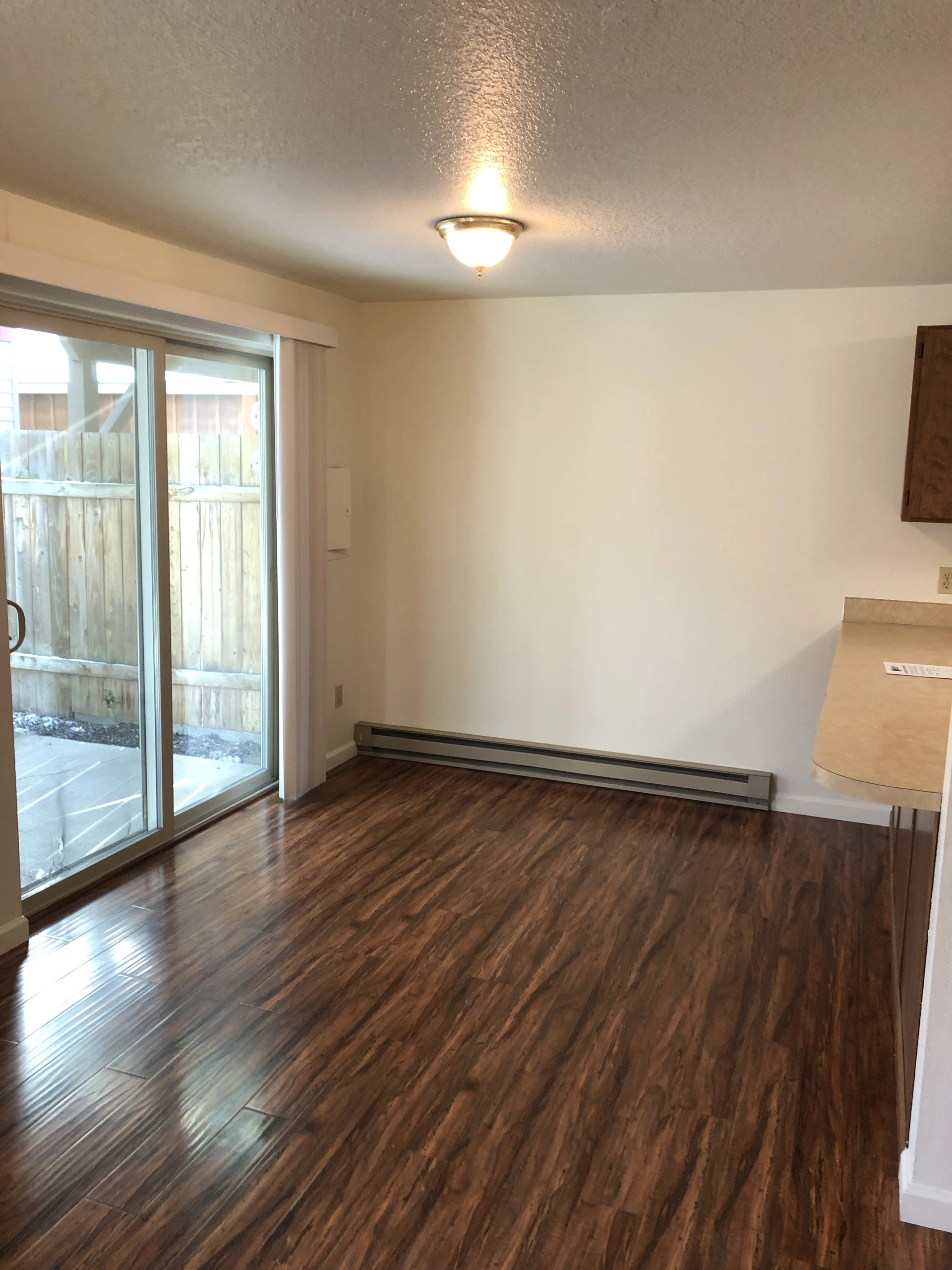 An empty room with dark wood-patterned flooring, a sliding glass door, a wall heater, and a lit ceiling fixture.